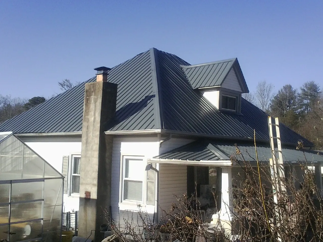 Dark blue standing seam metal roof on a white farmhouse with dormer — Slate & Tile Roof Repair by Roofing Brothers in Hollis Center