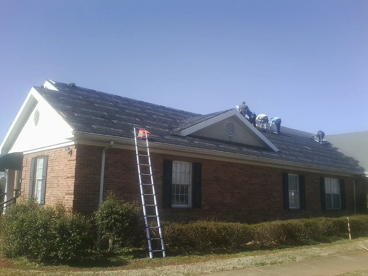 Crew tearing shingles off a brick ranch roof with a ladder set — Metal Roof Repair work by our crew in Hollis Center