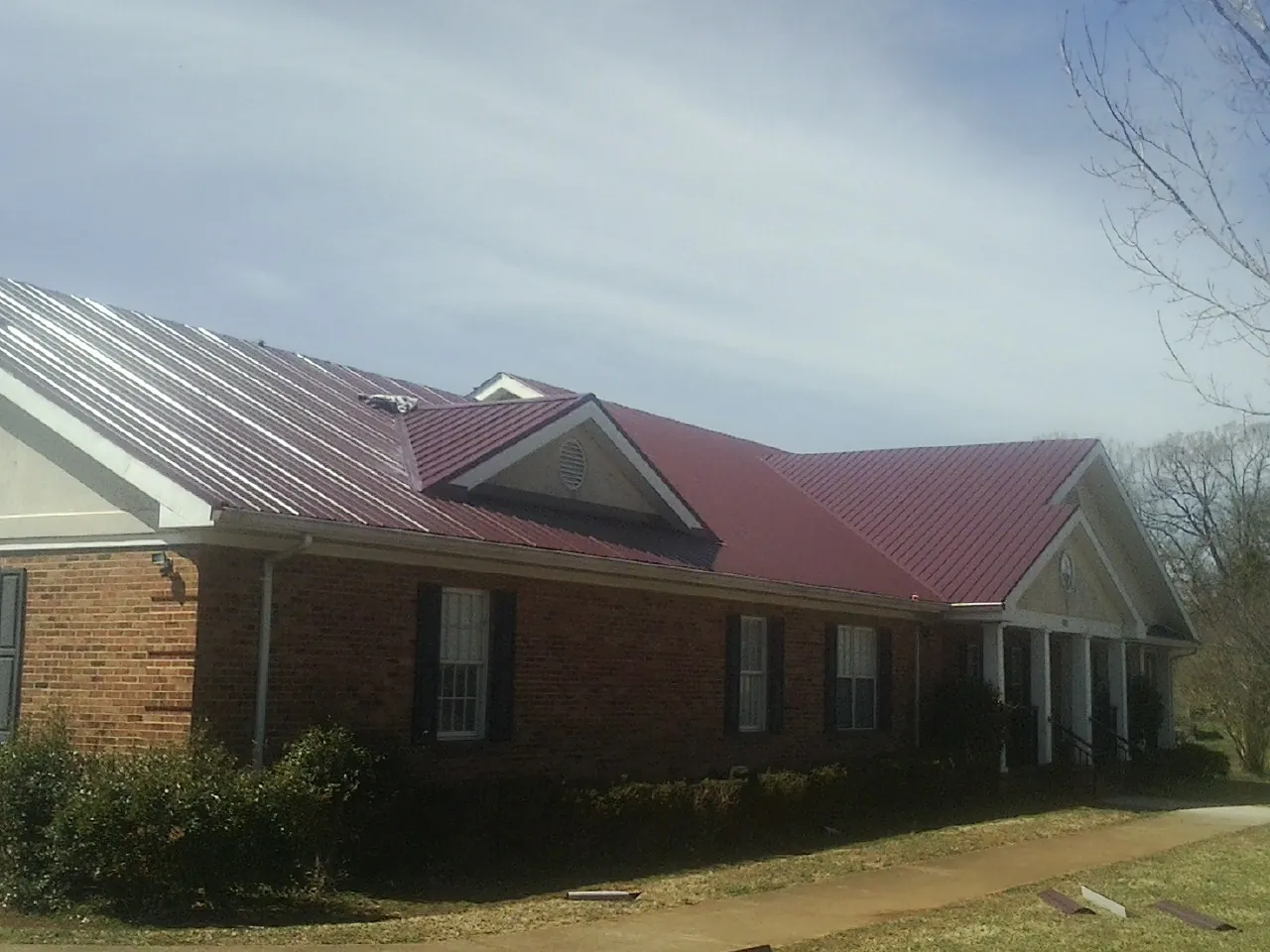 Red metal roof with gabled entries on a long brick building, from a Hail Damage Roof Repair job in Hollis Center