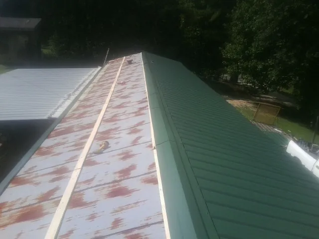 Old rusted panels beside newly installed green metal roofing — Wind Damage Roof Repair by Roofing Brothers in Hollis Center