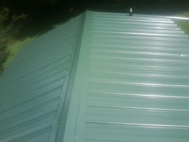 New green metal panels meeting at the ridge of a roof — Flat Roof Repair work by our crew in Hollis Center