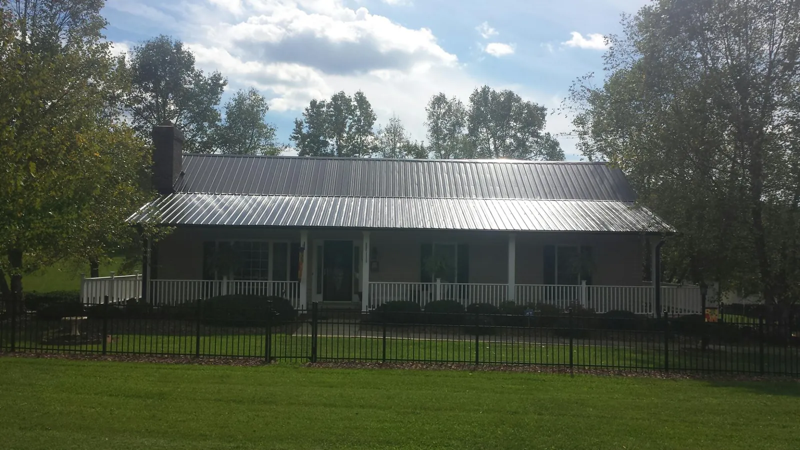 Gray metal roof on a brick ranch with a full width front porch — Gutter Guard Installation work by our crew in Hollis Center