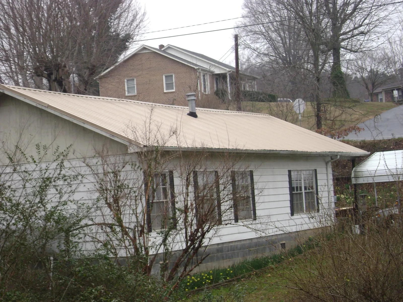 Tan metal roof on a white sided house set into a hillside — Commercial Roofing by Roofing Brothers in Hollis Center