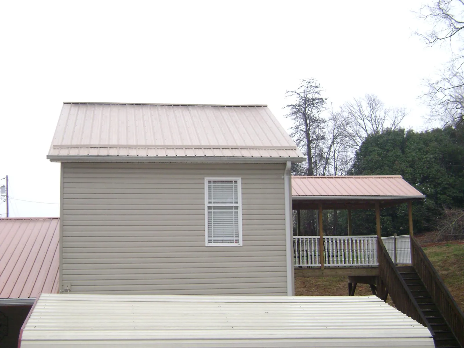 Tan metal roofs on a two story addition and attached porch, from a Roof Replacement job in Hollis Center